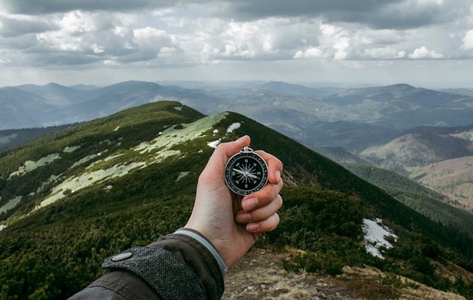 Taking Accurate Compass Bearing to Distant Mountain Landmark Hiker holding compass at proper chest height level position taking precise bearing measurement to mountain peak demonstrating correct technique for wilderness navigation and orienteering skills - InfoProds 2026