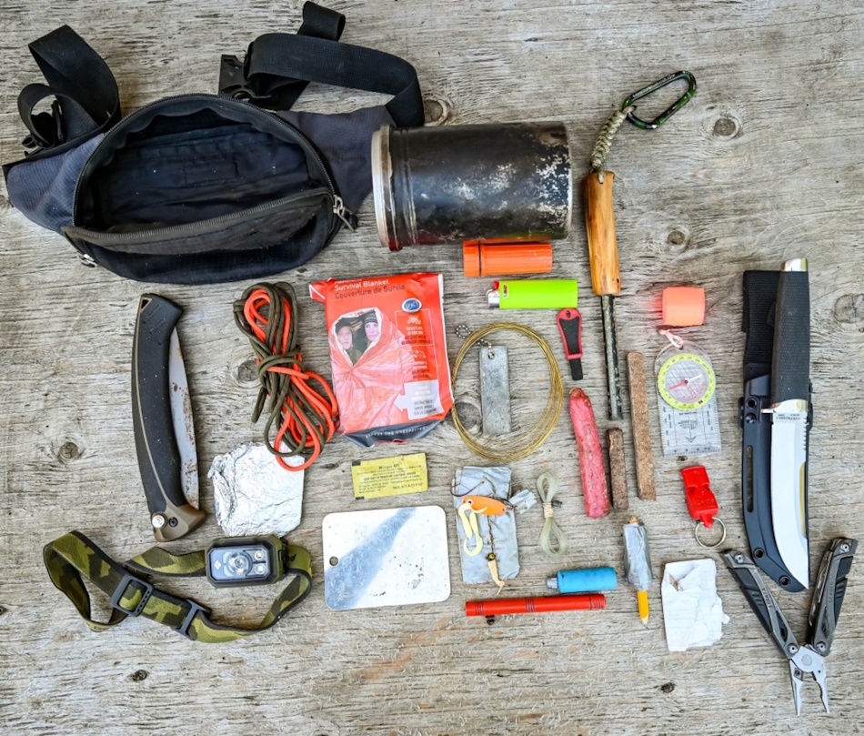 Comprehensive wilderness survival kit layout displaying the ten essentials including first aid supplies, emergency shelter, fire starting equipment, water purification, navigation tools, and signaling devices representing proper pre-trip preparation versus reliance on survival myths - InfoProds 2026