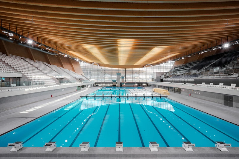 Olympic Swimming Pool Advanced Wave-Dampening Technology and Perforated Gutters Modern Olympic-standard swimming pool showing advanced perforated gutter systems and specialized lane ropes with wave-dampening technology designed for competitive swimming world record attempts - InfoProds 2026