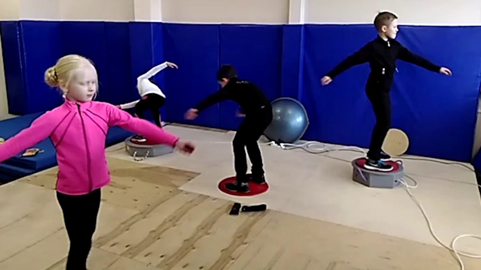 Elite Figure Skater Training on Motorized Rotation Equipment at Olympic Facility Olympic figure skating athlete performing specialized vestibular adaptation training on state-of-the-art motorized rotation platform with safety harness system at professional training center - InfoProds Athletic Training 2026