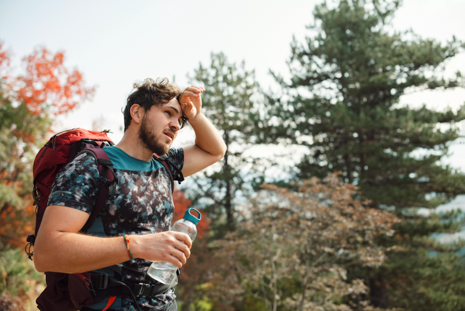Hiker experiencing heat exhaustion symptoms on summer trail Distressed hiker showing early heat exhaustion warning signs including headache and fatigue while sitting on rocky trail during summer hike, demonstrating critical importance of recognizing heat illness symptoms before progression to dangerous heatstroke - InfoProds 2026