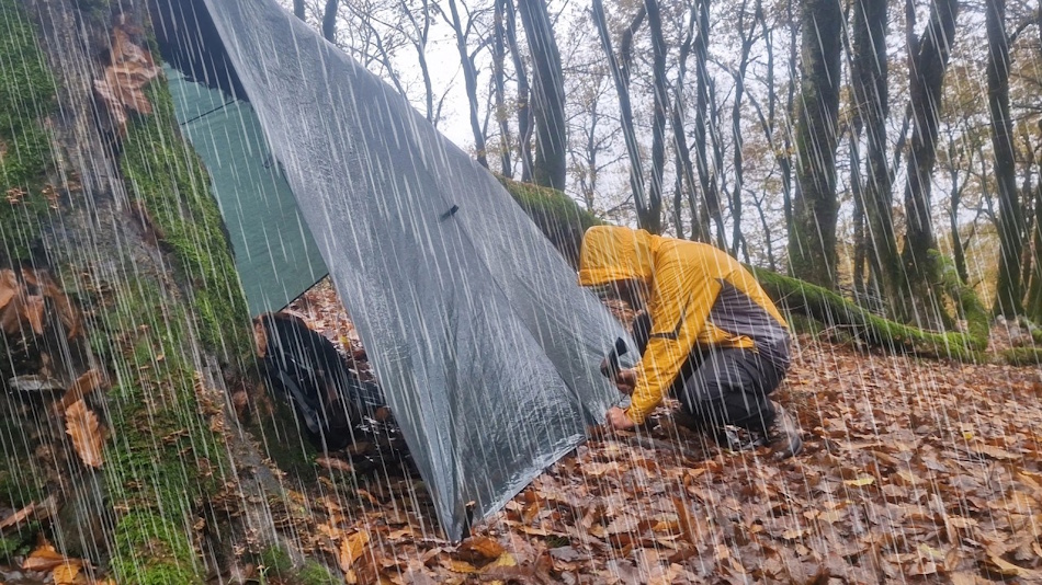 Survival Shelter Rain Testing Setup with Controlled Precipitation System Professional rain testing facility showing three different survival shelters including tarp, tent, and bivy sack positioned under controlled irrigation system simulating heavy rainfall conditions for comparative waterproof performance analysis - InfoProds Outdoor Survival Guide 2026