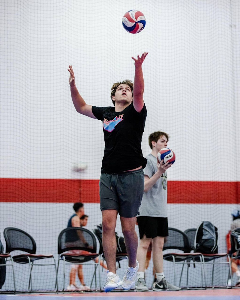A professional volleyball player in mid-air performing a jump serve while teammates stand in precise rotational zones on a blue court, illustrating 2026 tactical positioning - InfoProds 2026