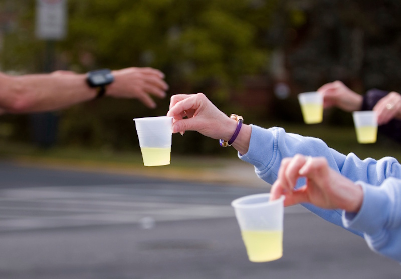 Marathon runner consuming energy gel and sports drink during race demonstrating proper mid-race fueling strategy with 60-90 grams carbohydrate hourly preventing glycogen depletion - InfoProds 2026