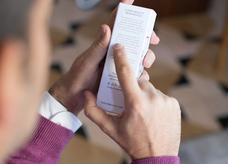 Person carefully reading cosmetic ingredient labels with magnifying glass examining chemical names to identify harmful ingredients and make informed safe beauty product choices - InfoProds 2026